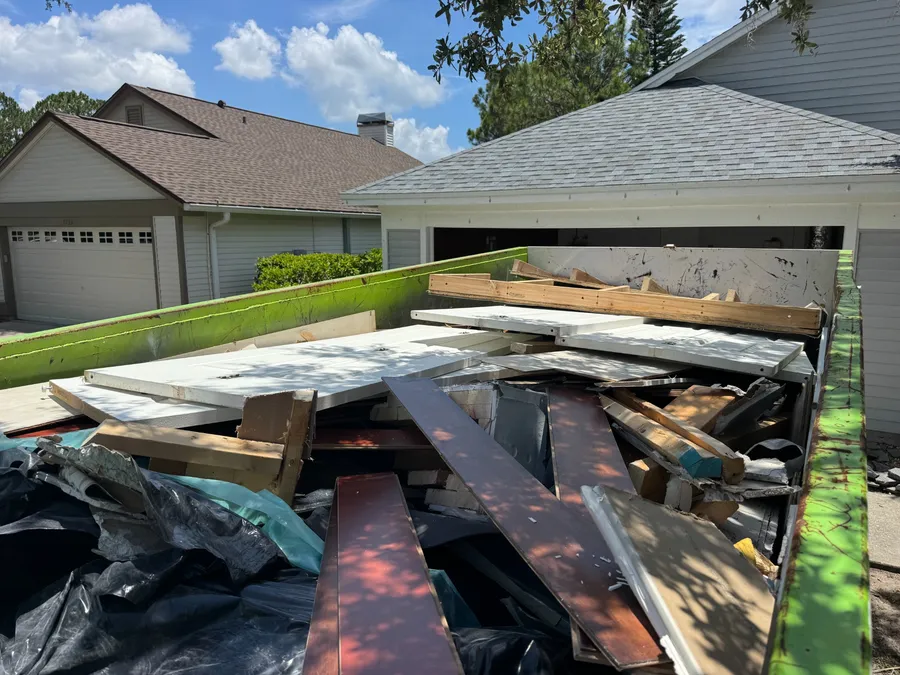 MAXCO roll-off dumpster in a home driveway loaded with doors, lumber and remodel debris