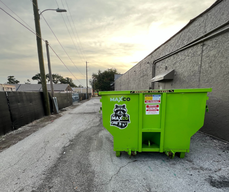 A green roll off dumpster sits in the back alley of a commercial property waiting to be loaded with construction debris.